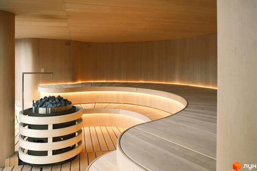 Інтер'єр сауни в котеджному містечку КМ Mountain Residence premium villas&spa з дерев'яними лавами та кам'яним обігрівачем. Затишна атмосфера з м'яким підсвічуванням.