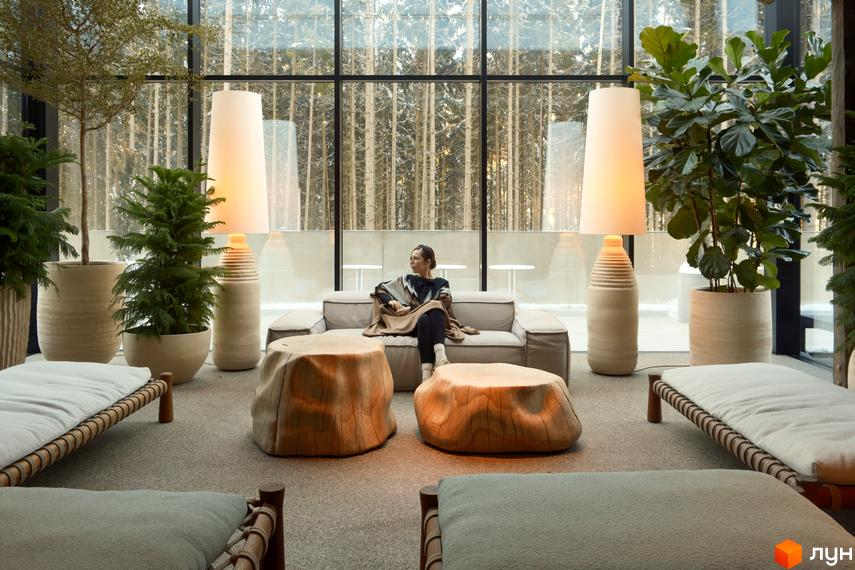 Інтер'єр вітальні в КМ Mountain Residence premium villas&spa з великими панорамними вікнами та природним освітленням. Затишна атмосфера з диваном, кріслами та рослинами.