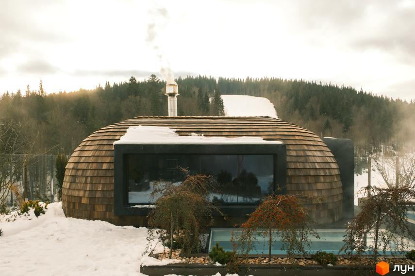 Котеджне містечко KM Mountain Residence premium villas&spa з дерев'яною сферою та панорамним вікном на тлі зимового лісу та басейну.