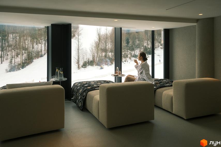 КМ Mountain Residence premium villas&spa: жінка в халаті п'є чай, насолоджуючись зимовим пейзажем з вікна спа-зони. Розкішний відпочинок серед гір.