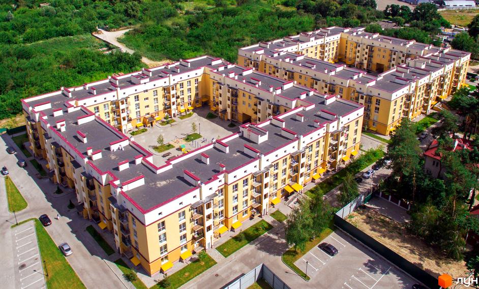 Житловий комплекс Сонцтаун: жовті багатоповерхові будинки з червоними дахами та білими елементами. На прибудинковій території розташовані паркувальні місця, зелені насадження та дитячий майданчик.