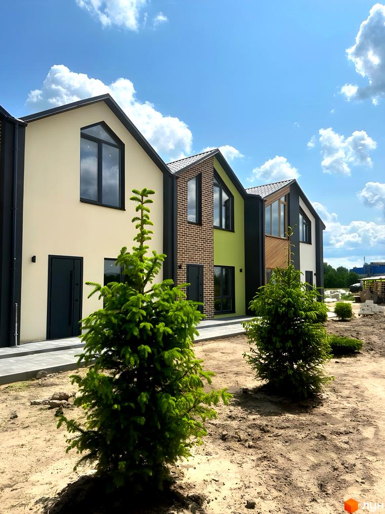 Зображення сторінки житлового комплексу Сітіхауси PRO MISTO. На фото ряд будинків з темними дахами та вікнами, перед будинками дерева та пісок.