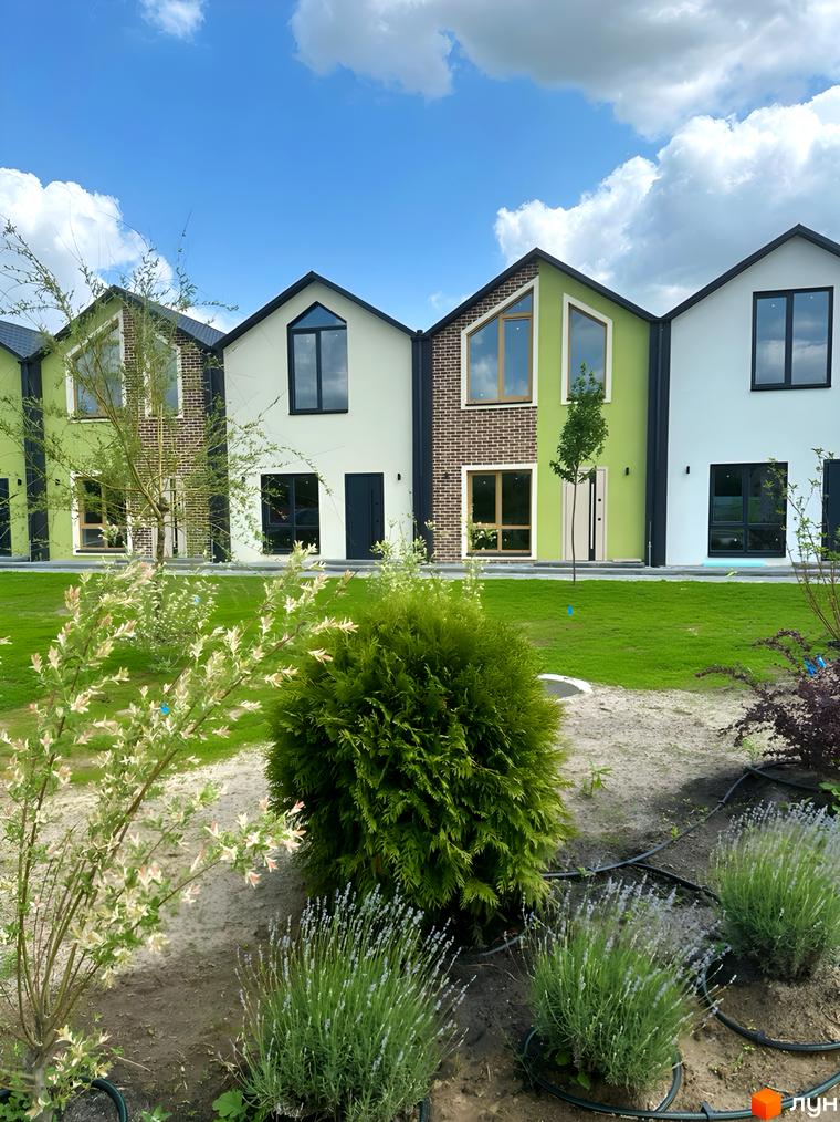 Зображення фасаду будинку житлового комплексу з зеленими стінами, панорамними вікнами та доглянутою прибудинковою територією з газоном та рослинами.