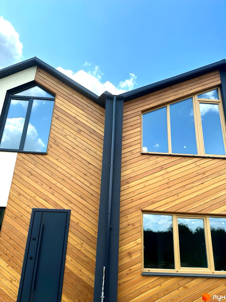 Зовнішній вигляд будинку Сітіхауси PRO MISTO з дерев'яним оздобленням фасаду та панорамними вікнами на тлі блакитного неба.