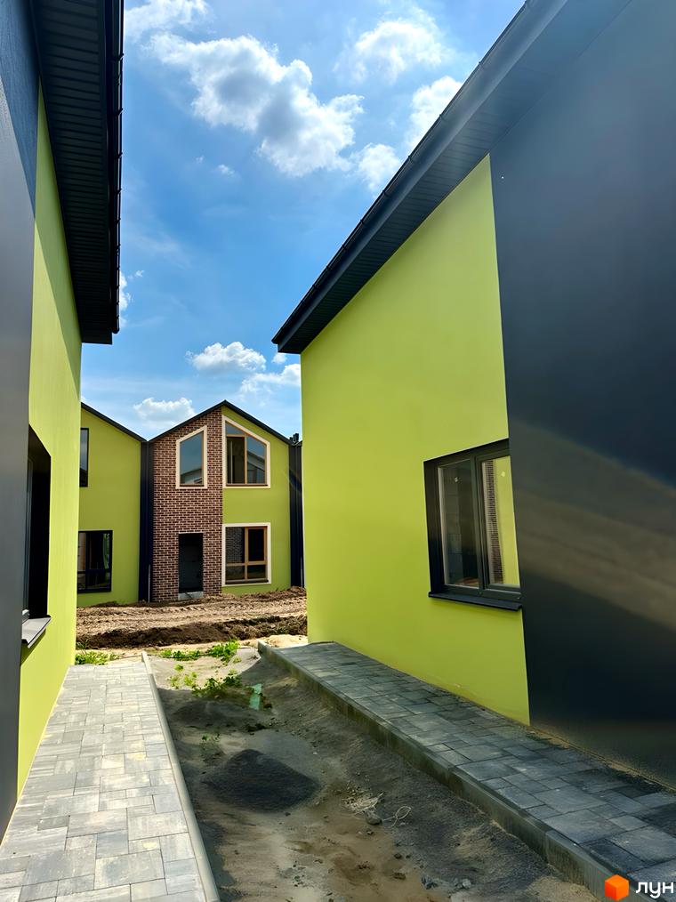 Зелені будинки з темними вікнами та дахом, між якими вимощена бруківкою доріжка, а посередині - земля. PRO MISTO.