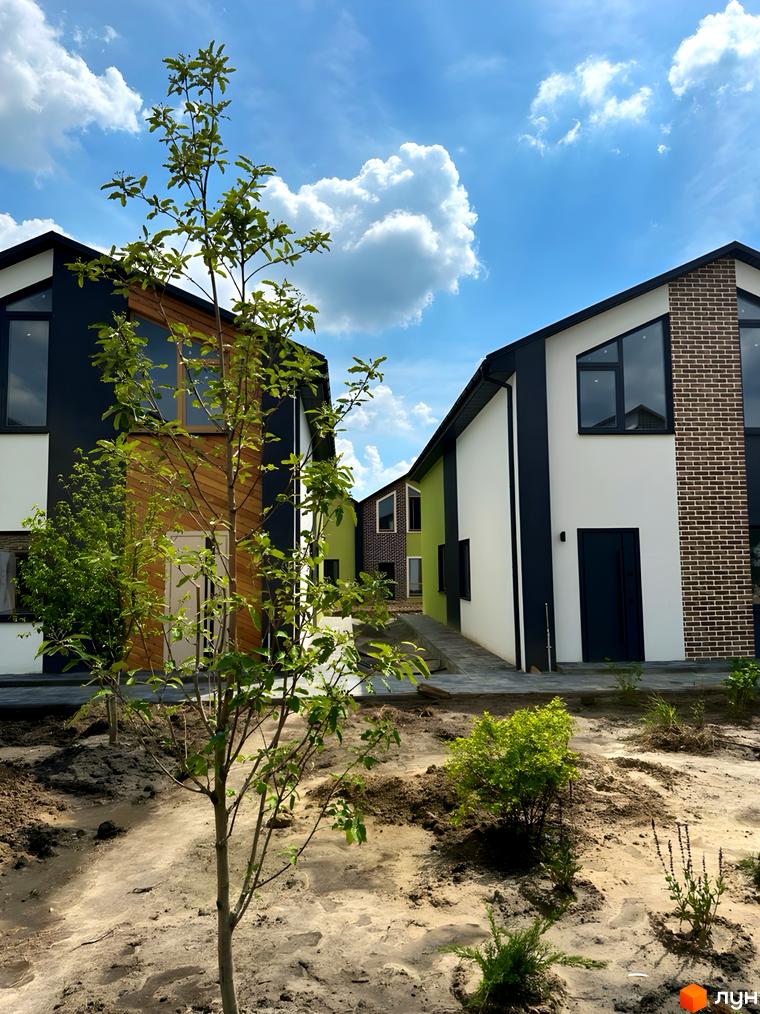 Зображення сторінки житлового комплексу Сітіхауси PRO MISTO. На фото будинки з білими та чорними фасадами, поруч молоді дерева та піщана територія.