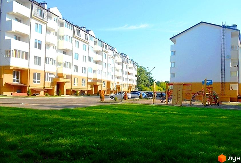 Зовнішній вигляд житлового комплексу Затишне містечко з білими фасадами та жовтими елементами, дитячим майданчиком та парковкою.