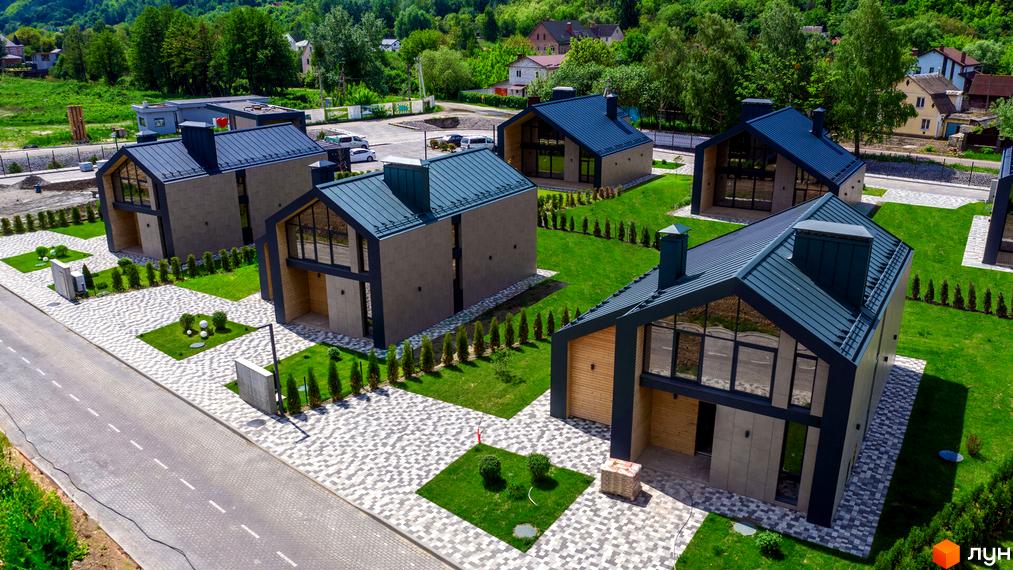 Котеджне містечко Piemont eco village: сучасні будинки з темними дахами та великими вікнами на тлі зелених пагорбів. Доглянута прибудинкова територія з бруківкою та газонами.