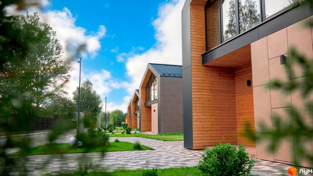 Котеджне містечко КМ Piemont eco village з дерев'яним фасадом та великими вікнами. Озеленена територія з бруківкою та сучасними ліхтарями.