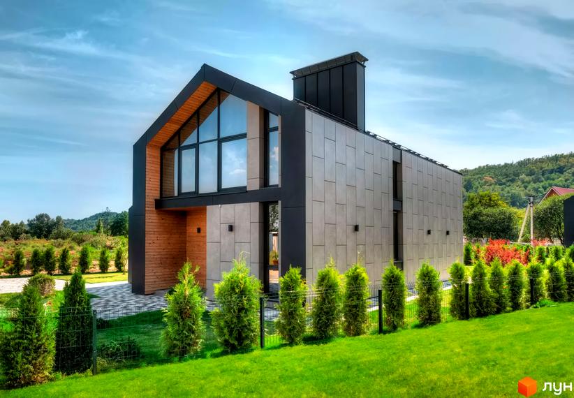 Котеджне містечко Piemont eco village: будинок з темним фасадом, дерев'яними вставками та великими вікнами. Перед будинком зелений газон з туями.