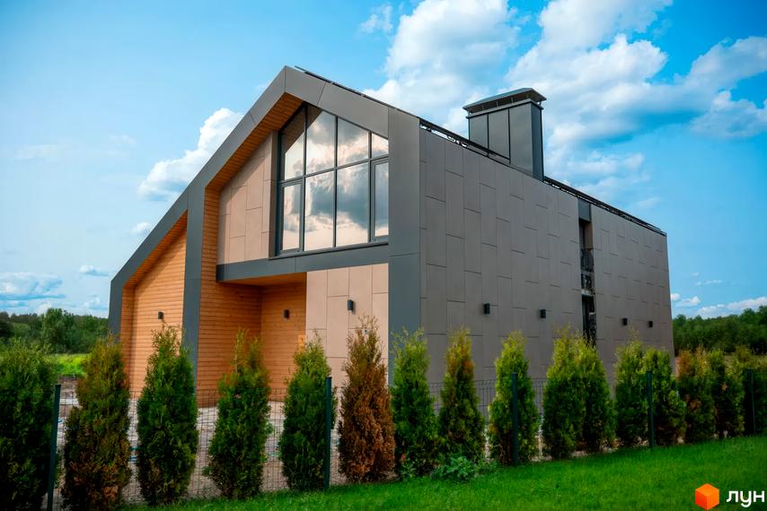 Котеджне містечко КМ Piemont eco village. Будинок з дерев'яним та сірим фасадом, великими вікнами, на фоні хмарного неба та зелених туй.