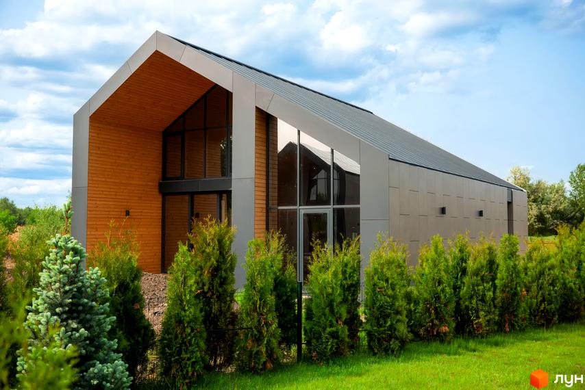 Котеджне містечко КМ Piemont eco village: двоповерховий будинок з дерев'яними та металевими елементами фасаду, великими вікнами та зеленою прибудинковою територією.
