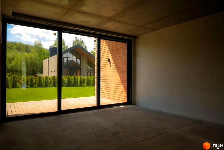 Котеджне містечко Piemont eco village: будинок з високим гострим дахом та панорамними вікнами, розташований серед зеленого газону та дерев.