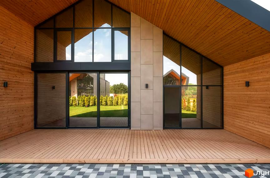 Фасад будинку Котеджного містечка Piemont eco village з дерев'яною обшивкою, панорамними вікнами та просторою терасою. Видно зелений двір.