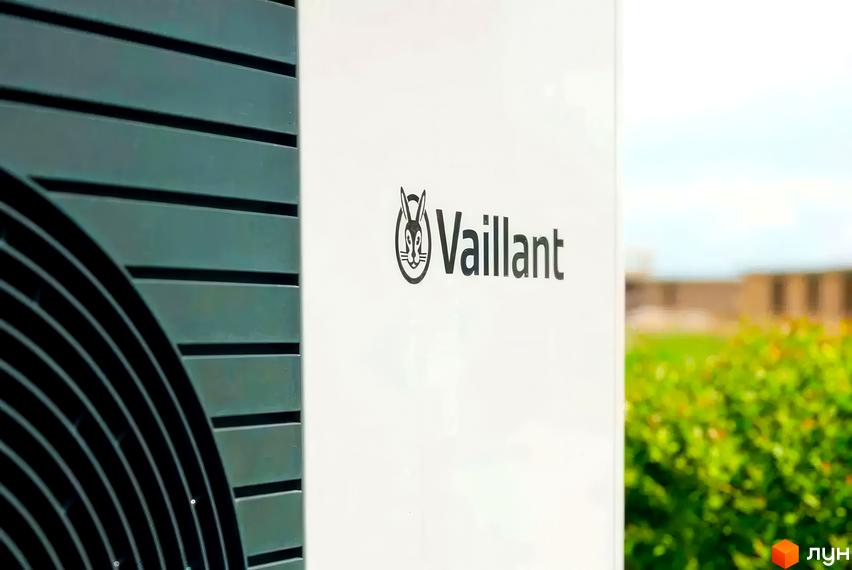 Зовнішній вигляд будинку з логотипом Vaillant. Навколо зелені кущі та будівлі.