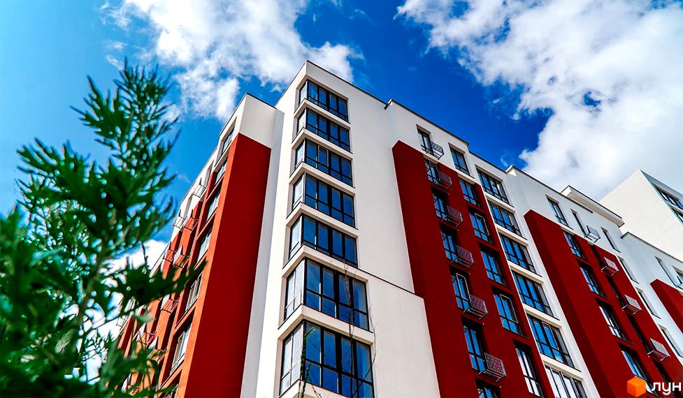Житловий комплекс Comfort House з червоно-білим фасадом та великими вікнами на тлі блакитного неба з хмарами. Зовнішній вигляд будівлі.
