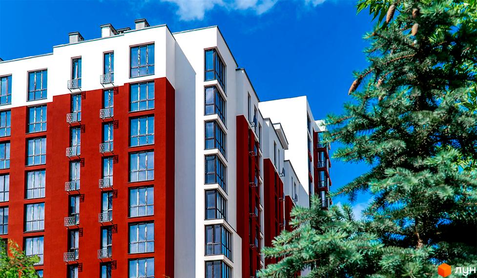 Житловий комплекс Comfort House з червоно-білим фасадом та великими вікнами. Навколо будівлі зелені дерева та блакитне небо.