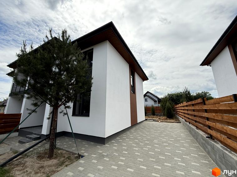 Зовнішній вигляд Котеджного містечка VillaTwins: двоповерховий будинок з білими стінами та коричневим дахом, поруч росте хвойне дерево, подвір'я вимощене плиткою.