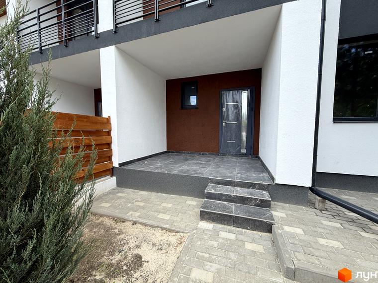 Вхідна група Котеджного містечка VillaTwins з білим та теракотовим фасадом, темними сходами та доріжкою з бруківки. Поруч зелені насадження.