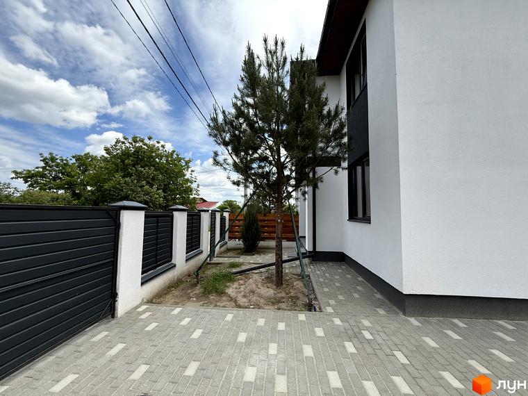 Білий будинок Котеджного містечка VillaTwins з темними вікнами та цоколем, доповнений сірим парканом та бруківкою.