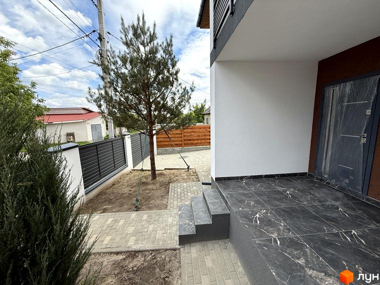 Зображення будинку та прибудинкової території Котеджного містечка VillaTwins. На подвір'ї росте дерево, викладена тротуарна плитка.