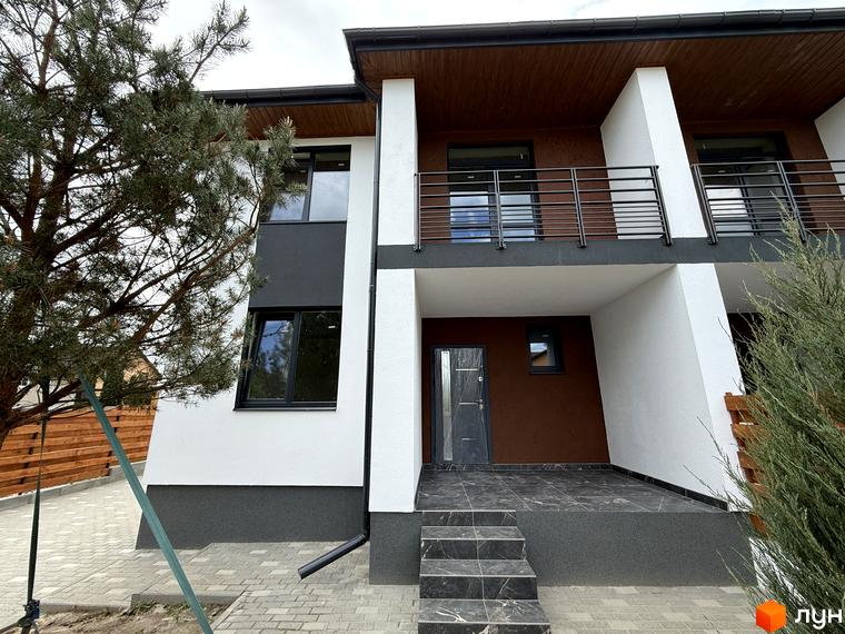 Котеджне містечко VillaTwins: двоповерховий будинок з білими та коричневими фасадами, чорними вікнами та балконом. Прибудинкова територія вимощена бруківкою, є дерева.