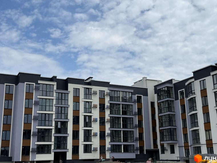 Зовнішній вигляд новобудови ЖК 9 Район, з великою кількістю вікон та балконів, на фоні хмарного неба.