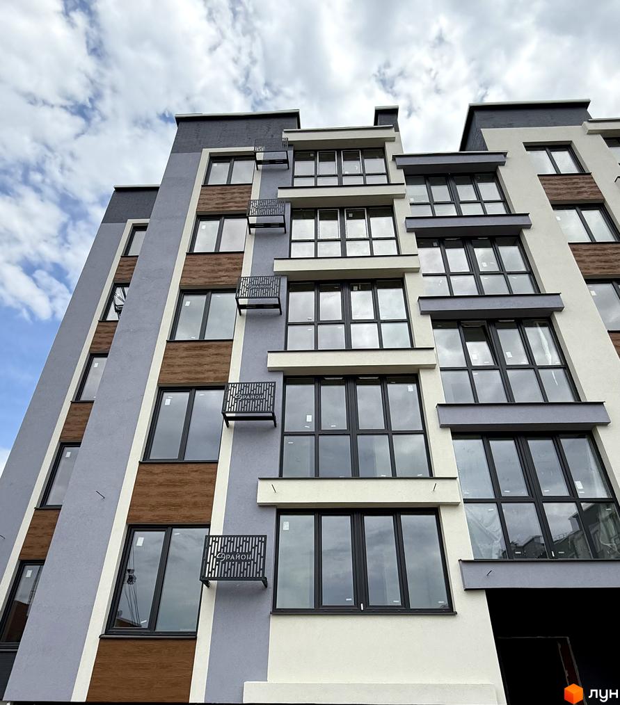 Зовнішній вигляд новобудови ЖК 9 Район з великими вікнами та балконами. Фасад будинку оздоблений сірими та дерев'яними елементами.