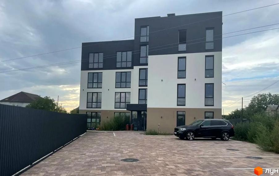 Новобудова на вулиці Шевченка з парковкою та парканом. Фасад будинку розділений на білі та чорні секції з великими вікнами.