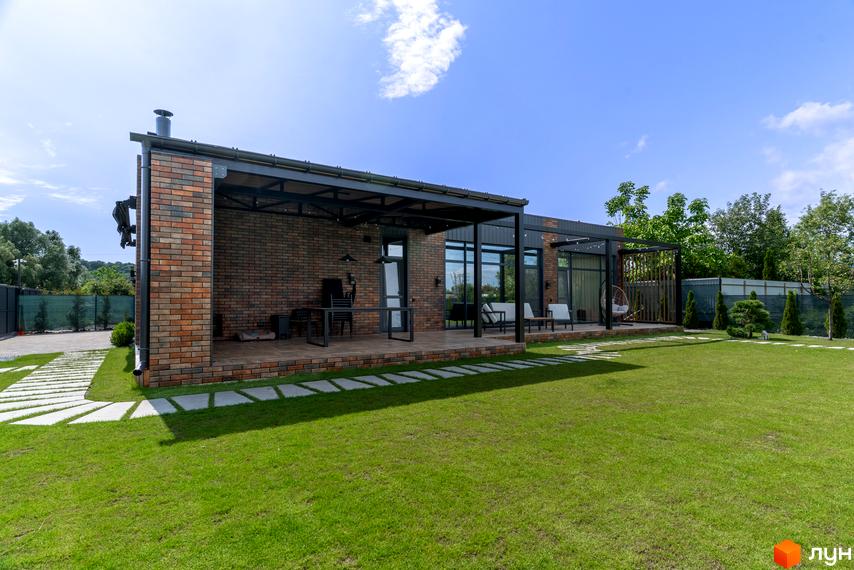 Котеджне містечко КМ Озерний: одноповерховий будинок з цегляним фасадом та терасою, доглянутий зелений двір з доріжками та рослинами.