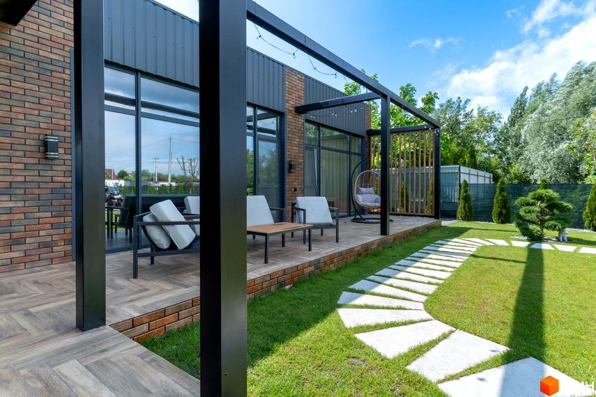 Зовнішній вигляд будинку КМ Озерний з терасою та зоною відпочинку. Прибудинкова територія з газоном та доріжкою з плитки.