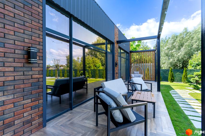 Котеджне містечко КМ Озерний: тераса з меблями та панорамними вікнами, зелена прибудинкова територія з доріжками.
