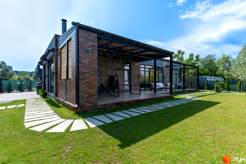 Котеджне містечко КМ Озерний: цегляний будинок з терасою та доглянутою зеленою ділянкою з доріжками з плитки.