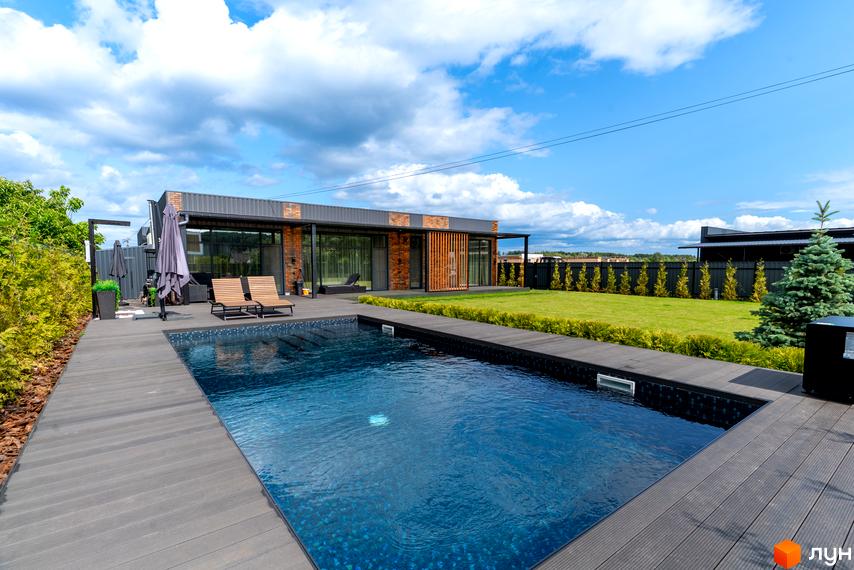 Котеджне містечко КМ Озерний. Будинок з цегляними та металевими елементами фасаду, великими вікнами та терасою. Прибудинкова територія з басейном, шезлонгами та доглянутим газоном.