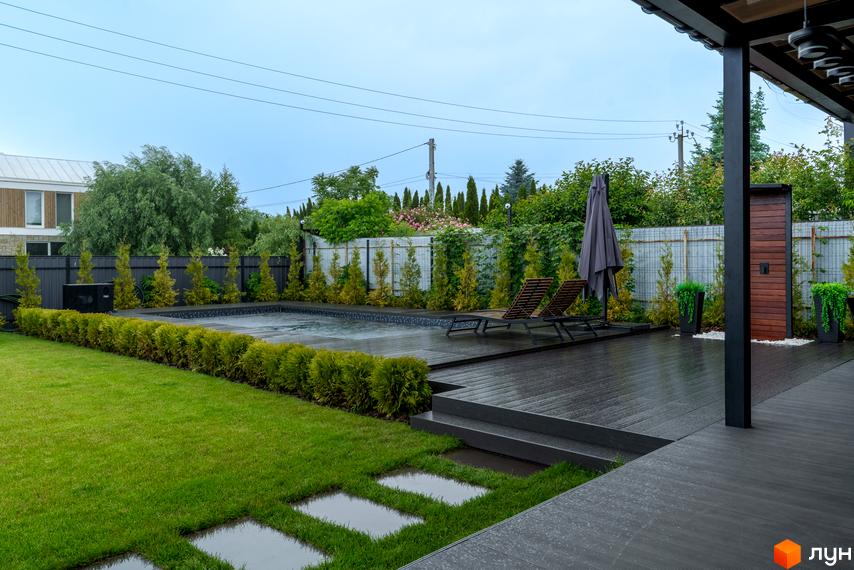 Котеджне містечко Озерний: сучасний задній двір з басейном, дерев'яною терасою, шезлонгами та парасолькою. Зелений газон з доріжками з плитки.