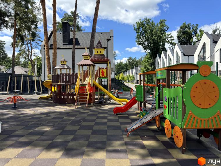 Котеджне містечко КМ Park Residence 3. Дитячий майданчик з гірками, потягом та іншими ігровими елементами на фоні будинків з двосхилими дахами.