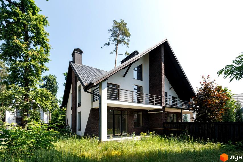 Котеджне містечко КМ Park Residence 3. Зовнішній вигляд будинку з цегляними вставками та великою терасою, оточений зеленню та травою.