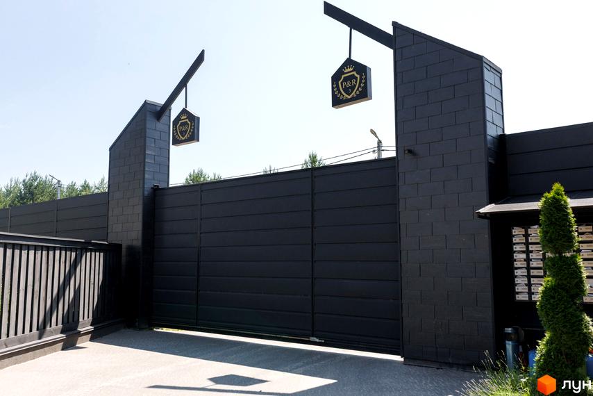 Котеджне містечко Park Residence 3: сучасний вхід з чорними воротами та парканом, прикрашений логотипом комплексу. Охайний ландшафт з туями та поштовими скриньками.