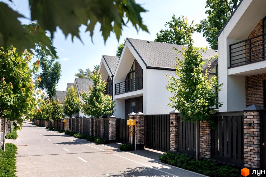 Котеджне містечко КМ Park Residence 3: сучасні будинки з цегляними елементами та акуратними парканами вздовж дороги. Зелені дерева та доглянута територія створюють затишну атмосферу.