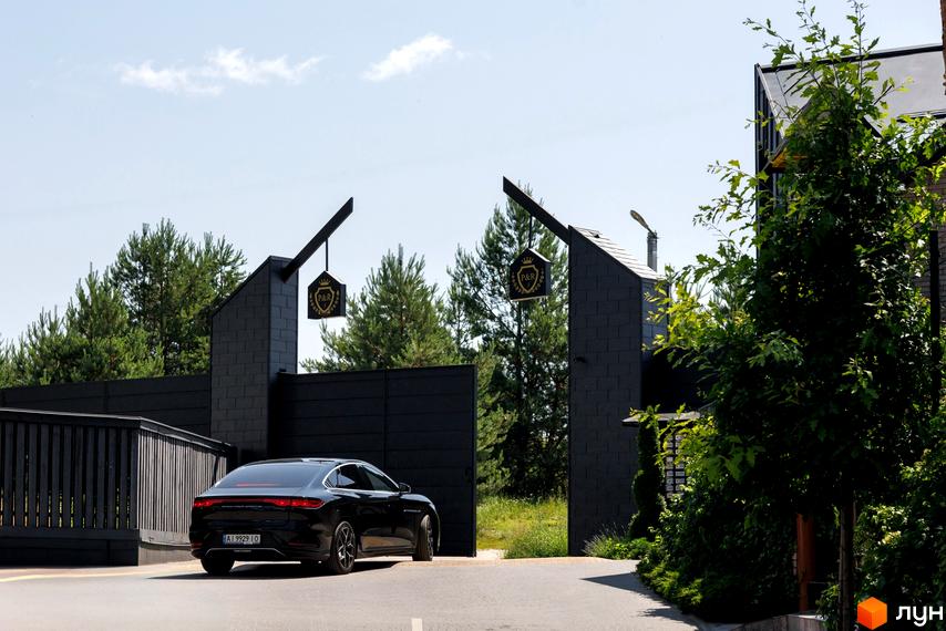 Котеджне містечко Park Residence 3: чорний фасад будинку, ворота, зелені насадження та автомобіль біля в'їзду.