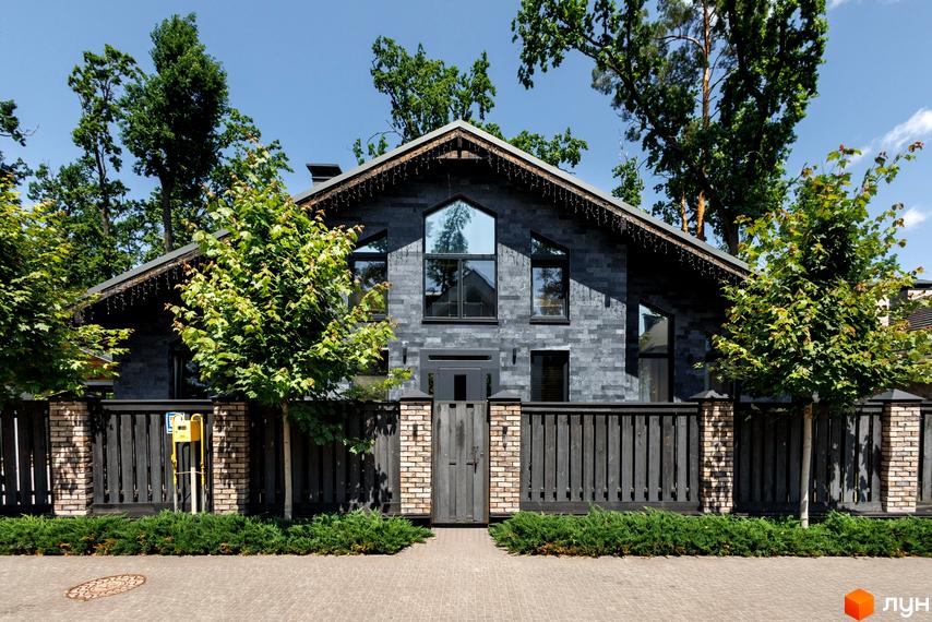 Котеджне містечко КМ Park Residence 3. Фасад будинку з сірої плитки, великі вікна, дерев'яна огорожа та зелені насадження.