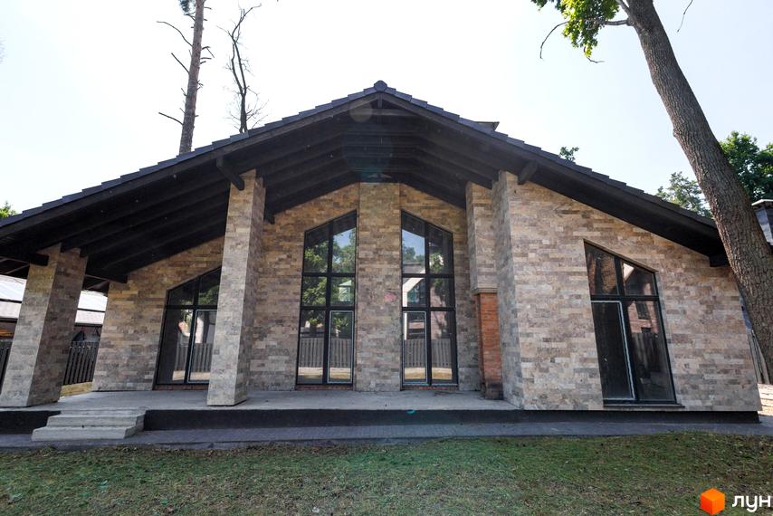 Котеджне містечко КМ Park Residence 3: фасад будинку з великими вікнами та кам'яною обробкою. Навколо будинку зелена галявина та дерева.