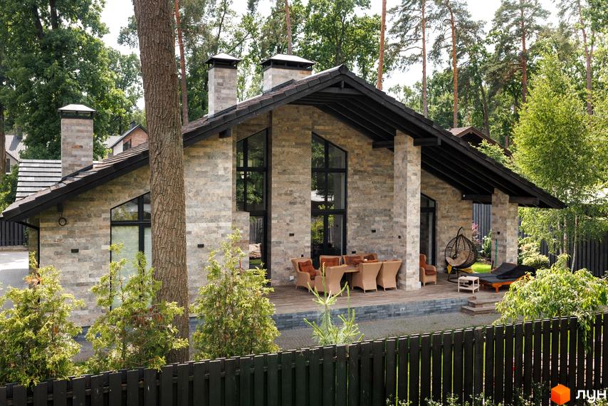 Котеджне містечко КМ Park Residence 3. Будинок з натурального каменю з великими вікнами та терасою з плетеними меблями.