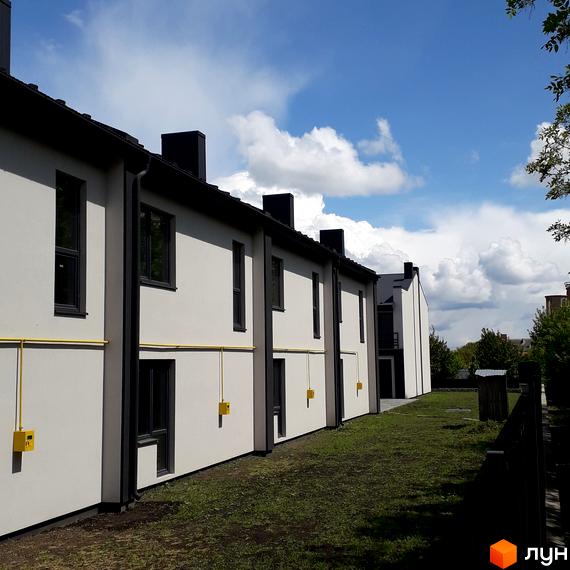 Зовнішній вигляд новобудови на вулиці Злагоди. Будинки з білими стінами та темними вікнами розташовані вздовж зеленої території.