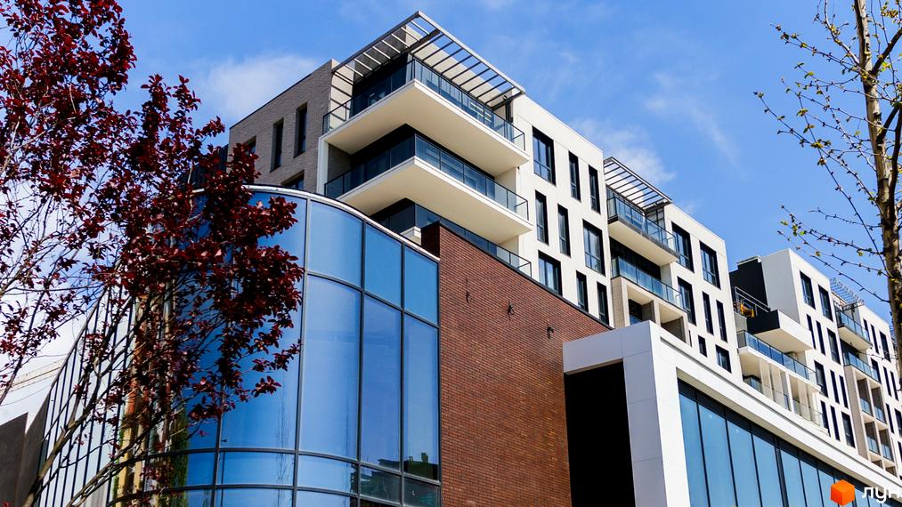 Зовнішній вигляд новобудови ЖК Grand Hills з панорамними вікнами та цегляною обробкою. Будинок має багатоповерхові балкони та сучасний дизайн фасаду.