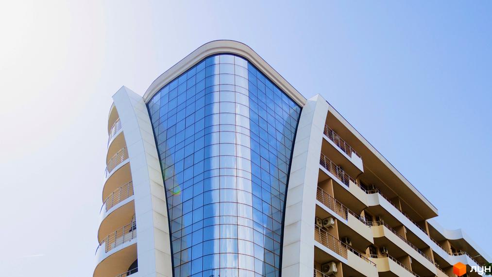 Житловий комплекс DREAM CITY з вигнутим скляним фасадом та балконами. Зовнішній вигляд новобудови з панорамним склінням та сучасними архітектурними елементами.