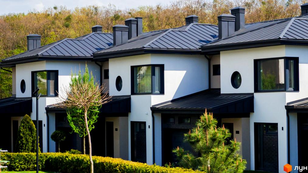 Котеджне містечко КМ SHERWOOD. Фасади будинків білого кольору з чорними елементами, металеві дахи та вікна. Навколо будинків зелені насадження та дерева.