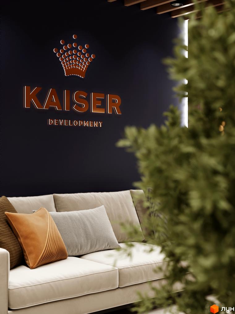 Вітальня зона в ЖК Kaiser Forest з диваном та подушками. На стіні логотип Kaiser Development та корона. Зелені рослини створюють затишну атмосферу.