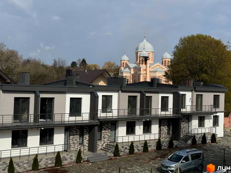 Вигляд на Котеджне містечко VIVA-CHERNIVTSI: двоповерхові будинки з балконами, акуратні зелені насадження, на фоні церква.