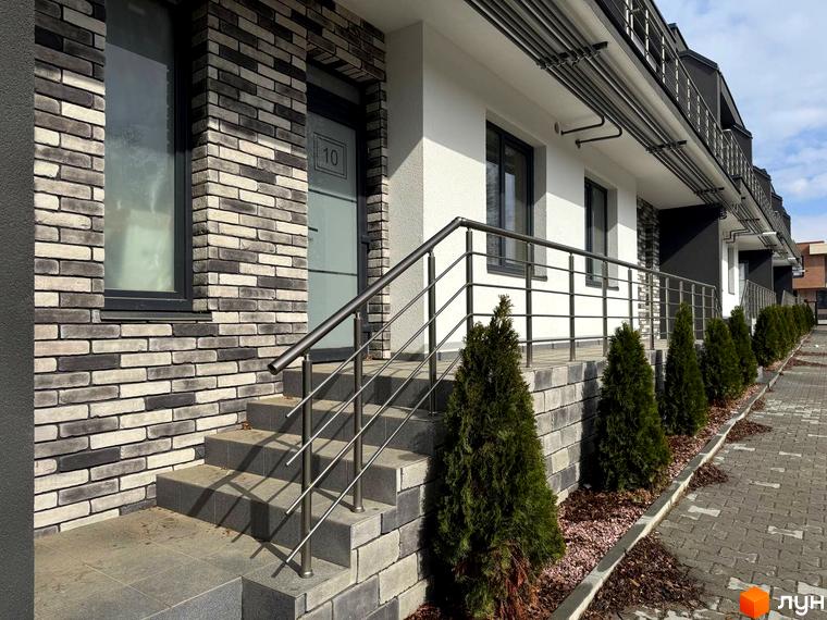 Зовнішній вигляд будинку в Котеджному містечку VIVA-CHERNIVTSI з цегляною кладкою та сходами. Навколо будинку висаджені декоративні дерева.